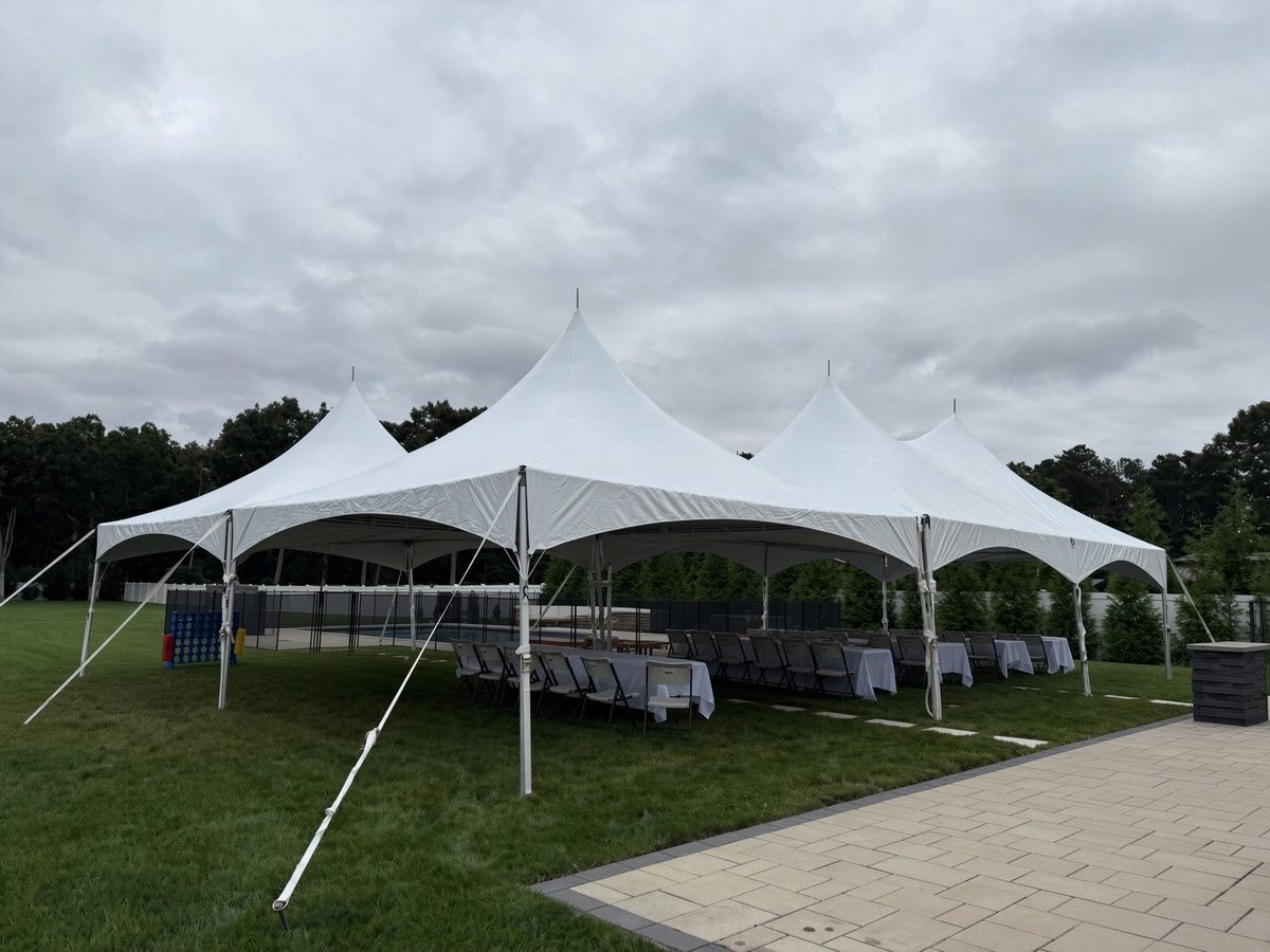 Large four-peak 20x40 frame tent beside a backyard pool with long tables dressed in white linens