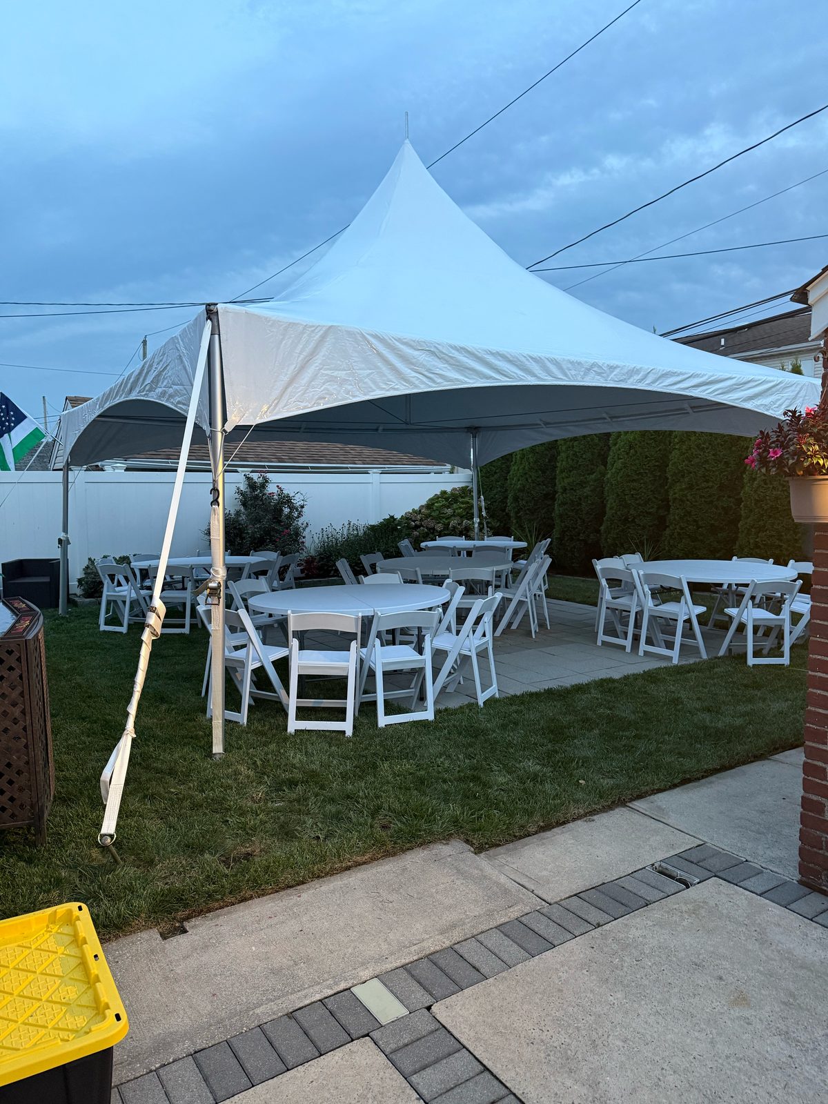 20x20 high peak tent at dusk with round tables and white wood-look folding chairs on a backyard lawn and patio
